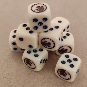 Könnte beinhalten: Eine Ansammlung elfenbeinfarbener Würfel mit dunkelblauen Augen und einem braunen Emblem auf jeder Seite. Die Würfel sind gestapelt und zeigen verschiedene Seiten. Geeignet für Brettspiele.