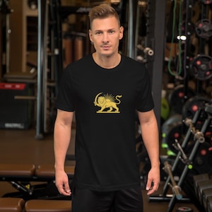 Op de afbeelding: Zwart t-shirt met een gouden embleem van een leeuw met een zwaard en een zon. Het embleem staat in het midden van de borst. Het t-shirt is gemaakt van een zacht materiaal en wordt in een sportschool gedragen.