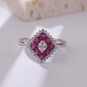 Puede incluir: Un anillo de plata con un engaste en forma de diamante que presenta un grupo de rubíes rojos rodeados de diamantes más pequeños.