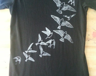 Könnte beinhalten: Schwarzes T-Shirt mit einem weißen Flockdruck eines Vogelschwarms, der diagonal fliegt.