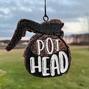 May include: A brown and black glitter coffee pot ornament with the words "POT HEAD" in white lettering.