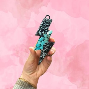 May include: A black lightning bolt shaped ornament with turquoise stones embedded in the design.