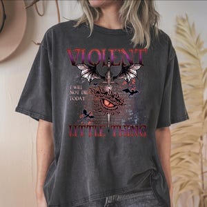 A person wearing a black t-shirt with a graphic design featuring a dragon, bats, and text that reads "I will not die today" and "Little thing".