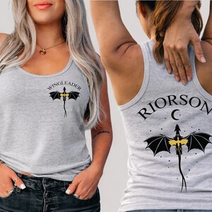 A woman wearing a grey tank top with a dragon design and the text "WINGLEADERRIOR C" printed on it.