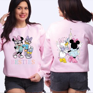 A woman wearing a pink sweatshirt with Minnie Mouse and other Disney characters printed on it.