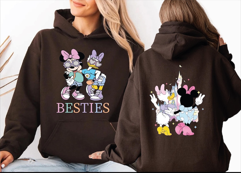 A woman wearing a brown hoodie with a graphic of Minnie Mouse and Donald Duck on the front, and the text "BESTIES" on the back.