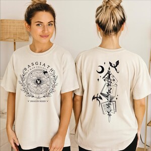 A woman wearing a white t-shirt with a graphic design on the front and a back featuring a black illustration of a dragon and a crescent moon.