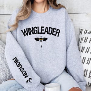 a woman sitting on a bed wearing a sweatshirt with the word wingleader on it