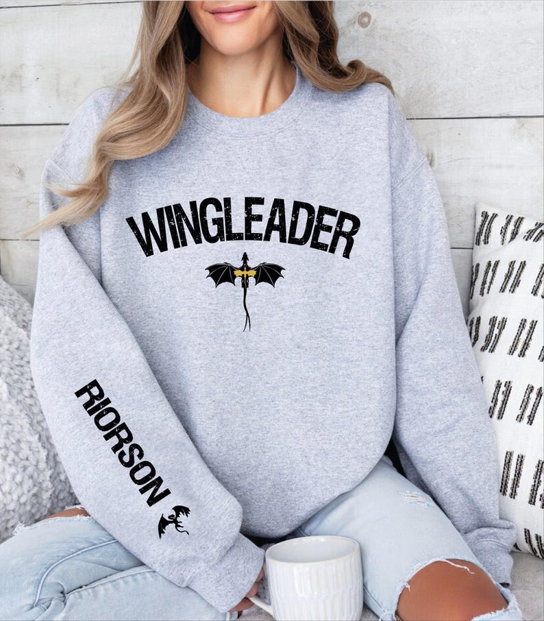 a woman sitting on a bed wearing a sweatshirt with the word wingleader on it