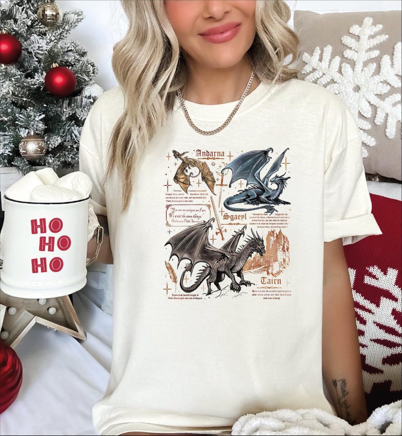 A woman wearing a white t-shirt with a graphic design of four dragons, including a dragon with a blue body and a dragon with a red body. She is holding a mug with the phrase "HO HO" written on it.