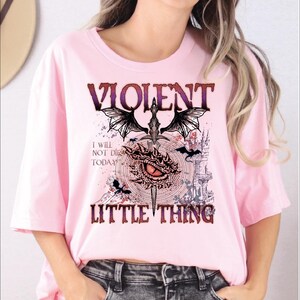 A woman wearing a pink t-shirt with a graphic design featuring a dragon, castle, and text.