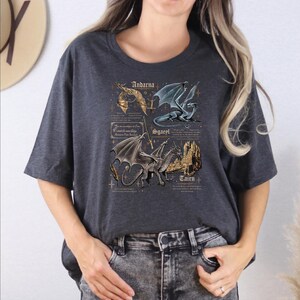 A woman wearing a gray t-shirt with a graphic design featuring a dragon and text related to the dragon.
