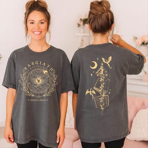 A woman wearing a grey t-shirt with a graphic design on the front and a back featuring a dragon and a crescent moon.