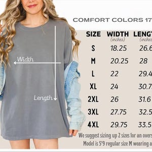a woman wearing a gray t-shirt with measurements and sizes listed below it.