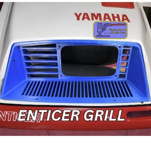 May include: A blue and white ENTICER GRILL, with the YAMAHA logo in red. The grill has a rectangular shape with a series of vertical and horizontal vents. The text "Winnipeg based 3D print Farm" is also visible.