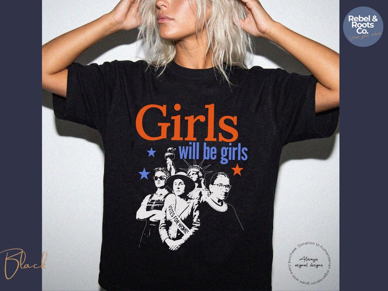 May include: Black t-shirt with the text "Girls will be girls" in orange and blue. The shirt features a graphic of several women, including the Statue of Liberty and Ruth Bader Ginsburg. The shirt is from Rebel & Roots Co.