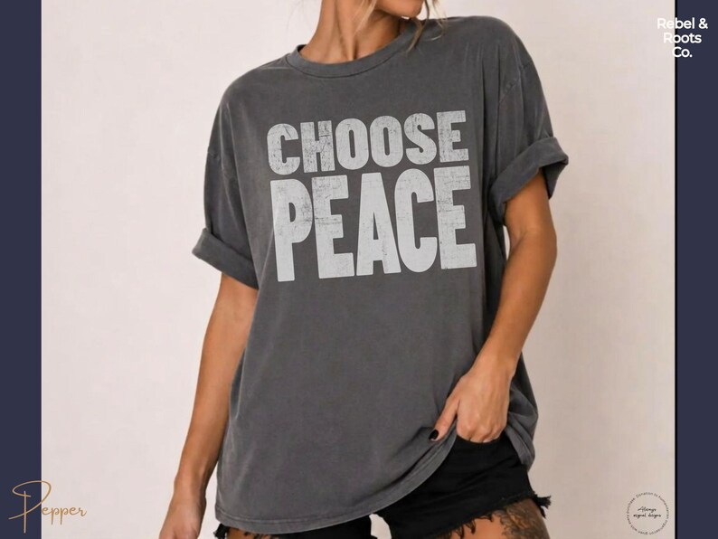 May include: A charcoal gray short-sleeve t-shirt with a distressed white graphic print on the front that reads CHOOSE PEACE in bold, capital letters. The garment features a crew neckline and a relaxed, loose-fitting silhouette with rolled sleeves.