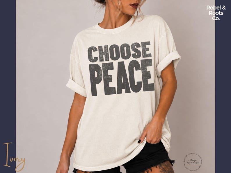 May include: An ivory short-sleeved t-shirt featuring the text CHOOSE PEACE in a distressed, dark gray, block-letter font. The shirt has a crew neckline and rolled sleeves, with a relaxed fit and a solid, light-colored base fabric.