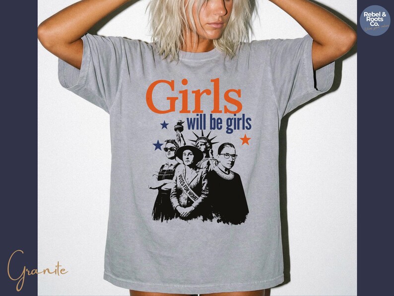 May include: Gray t-shirt with the text "Girls will be girls" in orange and blue. The shirt features a graphic of the Statue of Liberty and three women. The words "Votes for Women" are on a banner.