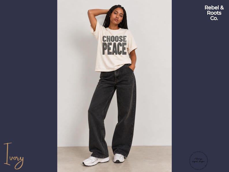 May include: An ivory short-sleeved t-shirt with the text CHOOSE PEACE printed in dark gray block letters on the chest, paired with loose-fitting charcoal gray denim jeans and white athletic sneakers with gray accents.