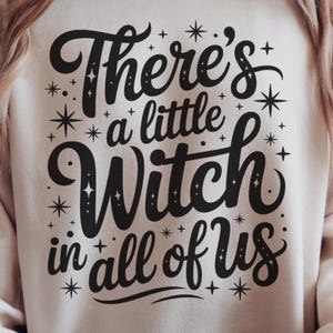 May include: Cream-colored sweatshirt with the phrase "There's a little Witch in all of us" in black script. The design includes star and dot accents, creating a whimsical, magical theme. Perfect for Halloween or everyday wear.