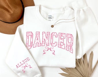May include: White sweatshirt with a pink floral design that says "Dancer" in a varsity style font. The left sleeve has the name "Allice" in pink with a pink bow.
