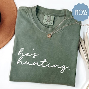 a t - shirt that says he's hunting next to a hat
