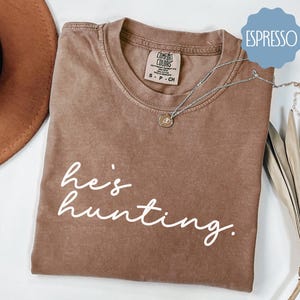 a t - shirt that says he's hunting next to a hat