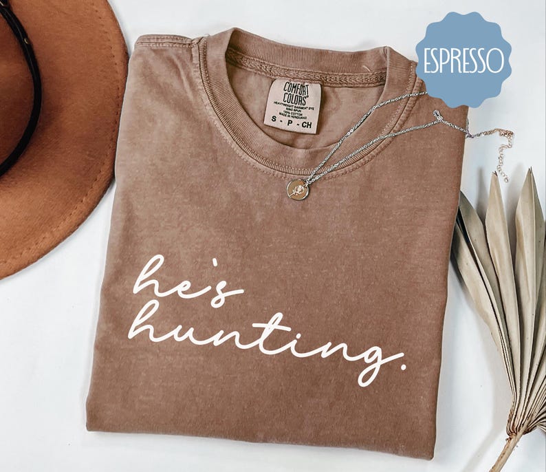 a t - shirt that says he's hunting next to a hat