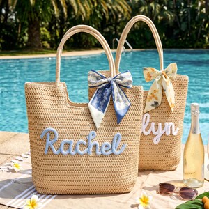 May include: Two woven straw tote bags with two handles each. One bag features the name Rachel in blue script, the other features the name lyn in white script. Both bags are decorated with a patterned fabric bow tied to one handle.