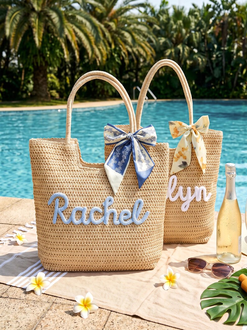 May include: Two woven straw tote bags with two handles each. One bag features the name Rachel in blue script, the other features the name lyn in white script. Both bags are decorated with a patterned fabric bow tied to one handle.