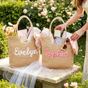 May include: Two woven straw tote bags featuring personalized names in script lettering. One bag displays the name Evelyn in white, while the other displays the name Sophia in pink. Both bags are filled with various small gift items and accessories.