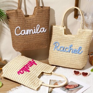 May include: Three woven straw tote bags with two top handles each. One tan bag features the white embroidered name Camila. One light beige bag features the blue embroidered name Rachel. One light beige bag features the pink embroidered name Amelia.