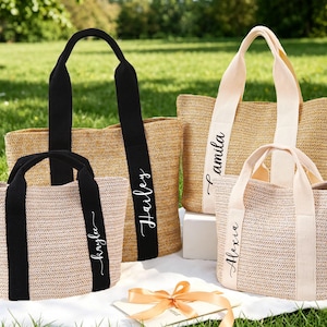 Puede incluir: Una taza de cerámica blanca con un asa negra y el texto "But First, Coffee" en negrita negra. La taza se encuentra sobre un fondo borroso, sugiriendo un ambiente acogedor.