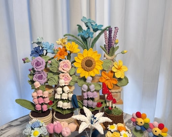 以下が含まれることがあります： 小さな鉢植えに入った、カラフルなかぎ針編みの花々のコレクション。ひまわりやバラなど、様々な種類の花が木製の棚に並んでいます。鉢には装飾的なレースのトリムが付いています。