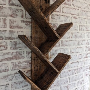May include: A dark brown wooden wall shelf with five angled shelves. The shelf is mounted on a white brick wall.