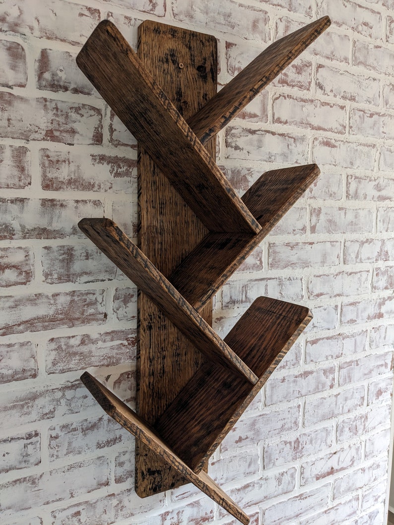 May include: A dark brown wooden wall shelf with five angled shelves. The shelf is mounted on a white brick wall.