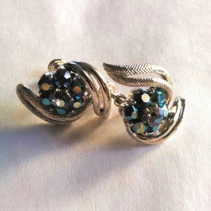 May include: A pair of silver tone clip-on earrings with a cluster of blue and white rhinestones in a swirl design.
