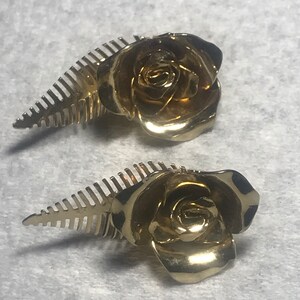 May include: A pair of gold-tone rose hair clips with a leaf design. The roses are detailed and realistic.