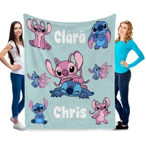 K&ouml;nnte beinhalten: Eine hellblaue Decke mit den Zeichentrickfiguren Stitch und Angel in verschiedenen Posen. Auf der Decke stehen die Namen "Clar&aacute;" und "Chris". Die Decke wird von zwei Personen gehalten.