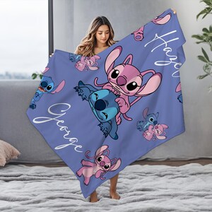 K&ouml;nnte beinhalten: Eine periwinkleblaue Decke mit den Zeichentrickfiguren Stitch und Angel in verschiedenen Posen. Die Decke tr&auml;gt die Namen "George" und "Hayley" in wei&szlig;er Schrift. Die Decke besteht aus einem weichen Material.