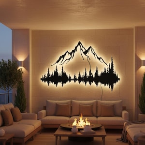 Può includere: Un'opera d'arte da parete in metallo nero con silhouette di montagna e foresta con illuminazione a LED bianca calda integrata. L'opera è montata su una parete beige sopra un divano, creando un accogliente spazio abitativo all'aperto. La scena include un braciere e mobili in legno.