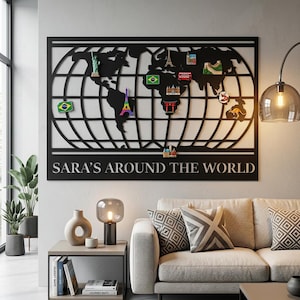 May include: Black metal world map wall art with a grid design and the text "SARA'S AROUND THE WORLD". The map features colourful magnets representing landmarks and flags, including the Eiffel Tower and the Statue of Liberty. The artwork is displayed above a sofa.