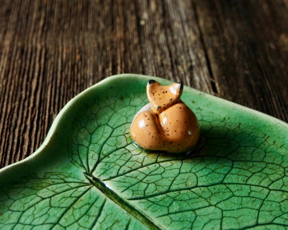 A hand-sculpted ceramic plate shaped like a leaf with a fox relief — functional art that doubles as a conversation-starting desk or kitchen tray, and 13 favorites signal real organic interest.
