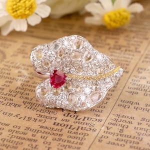 Könnte beinhalten: Ein filigraner Ring in Blattform mit einem großen Rubin-Edelstein in der Mitte, umgeben von kleineren Diamanten und einem dünnen Band aus Gelbgold.