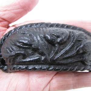 Pode incluir: Puxador de gaveta de ferro fundido preto com um design de corda ao redor da borda e um design floral no centro.