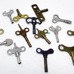 May include: A collection of various metal clock winding keys in assorted shapes and sizes. The keys are finished in silver, brass, and dark tones, featuring butterfly-style handles and cylindrical shafts for winding mechanical timepieces.
