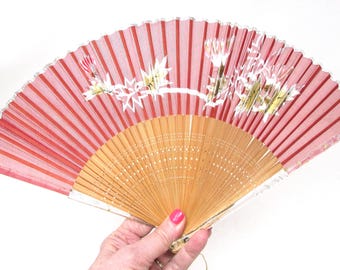 Abanico plegable vintage: diseño floral plateado sobre seda rosa, marco de madera.