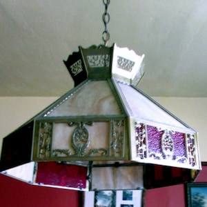 May include: A vintage, octagonal, stained glass ceiling light fixture with a brass frame and a white and red glass design. The light fixture is hanging from a chain.