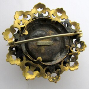 May include: Gold-toned brooch with a round, black cameo set in a filigree frame. The brooch has a pin and catch closure on the back.